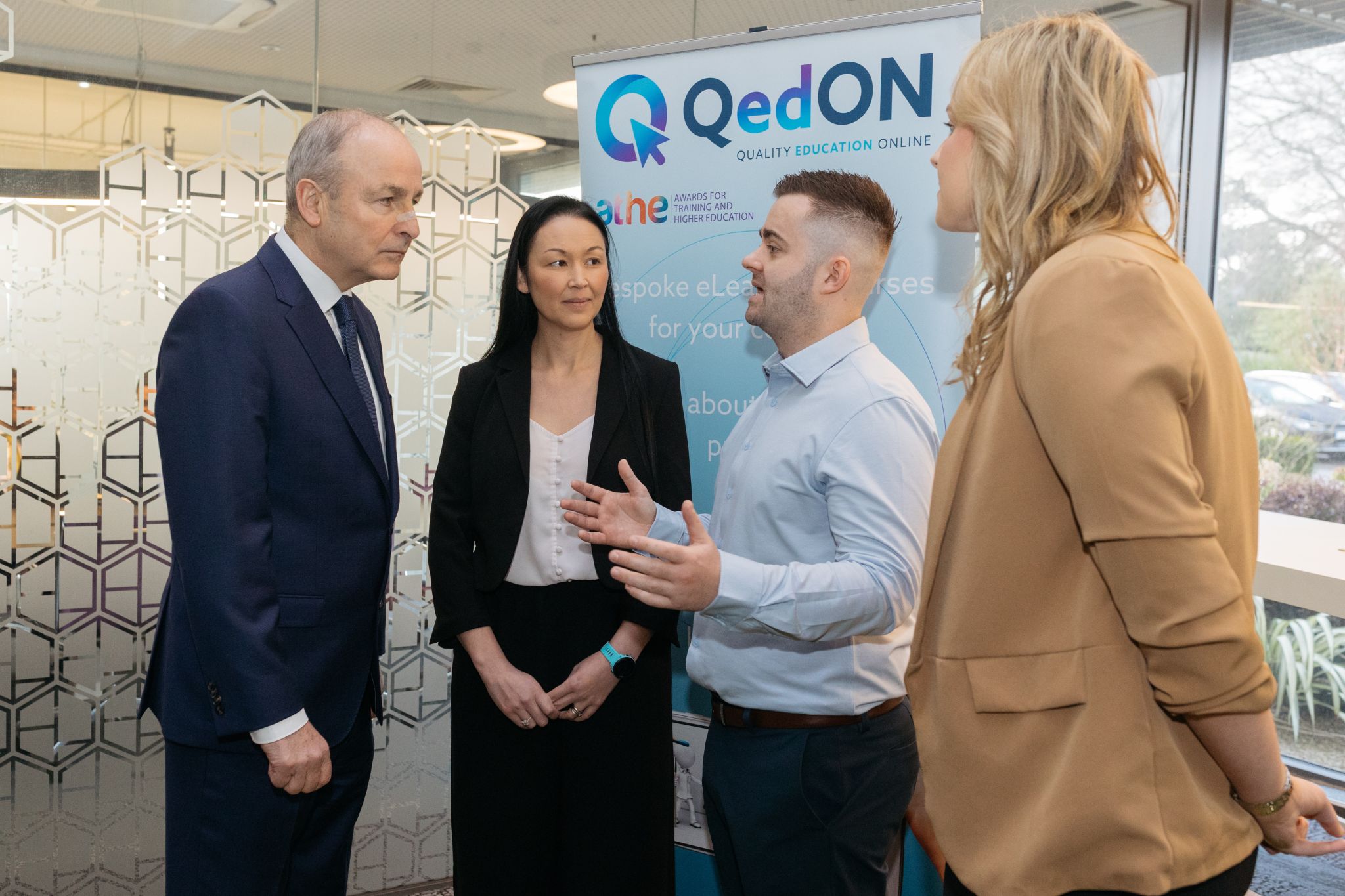 Ireland's Taoiseach with QedON team members at The Hatch Lab, standing beside a QedON banner